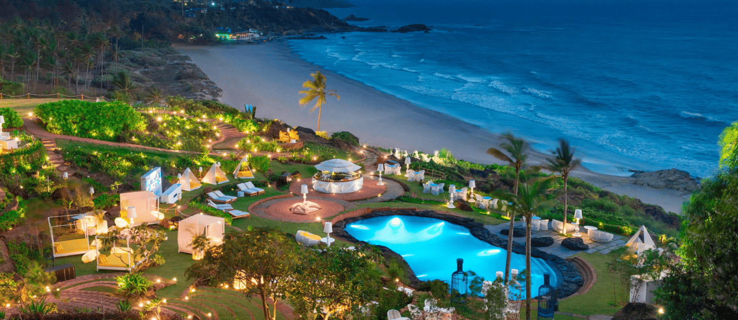 A colorful night market street with shops displaying clothes and a sign for Wind Horse Tattoo Studio.